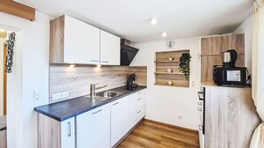 Une cuisine de taille réduite avec des meubles blancs, un plan de travail en bois, un évier et une machine à café.