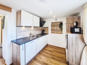 Una cocina compacta con armarios blancos, una encimera de madera, un fregadero y una cafetera.