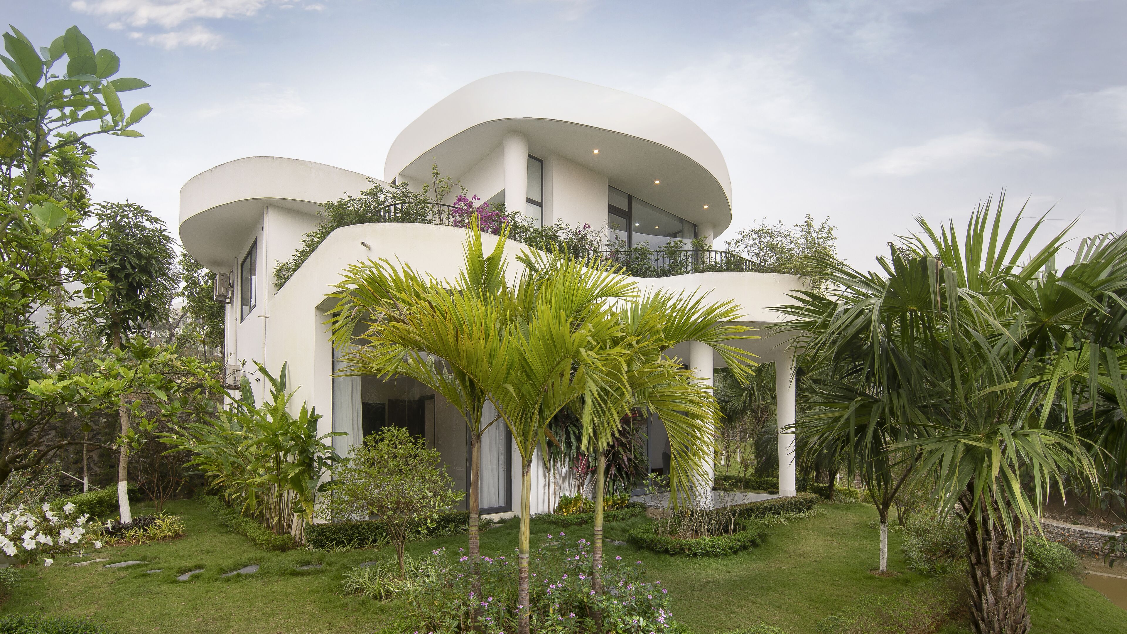 Un edificio moderno con una arquitectura curva distintiva, rodeado de exuberante vegetación y un jardín cuidado.