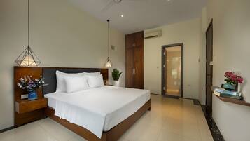 A modern hotel bedroom with a large bed, wooden headboard, bedside tables with lamps, an air conditioning unit, and a door leading to another room.