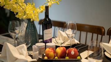 A dining table with a bottle of Chateau Dalat wine, three glasses, a vase with yellow flowers, and a plate with apples.