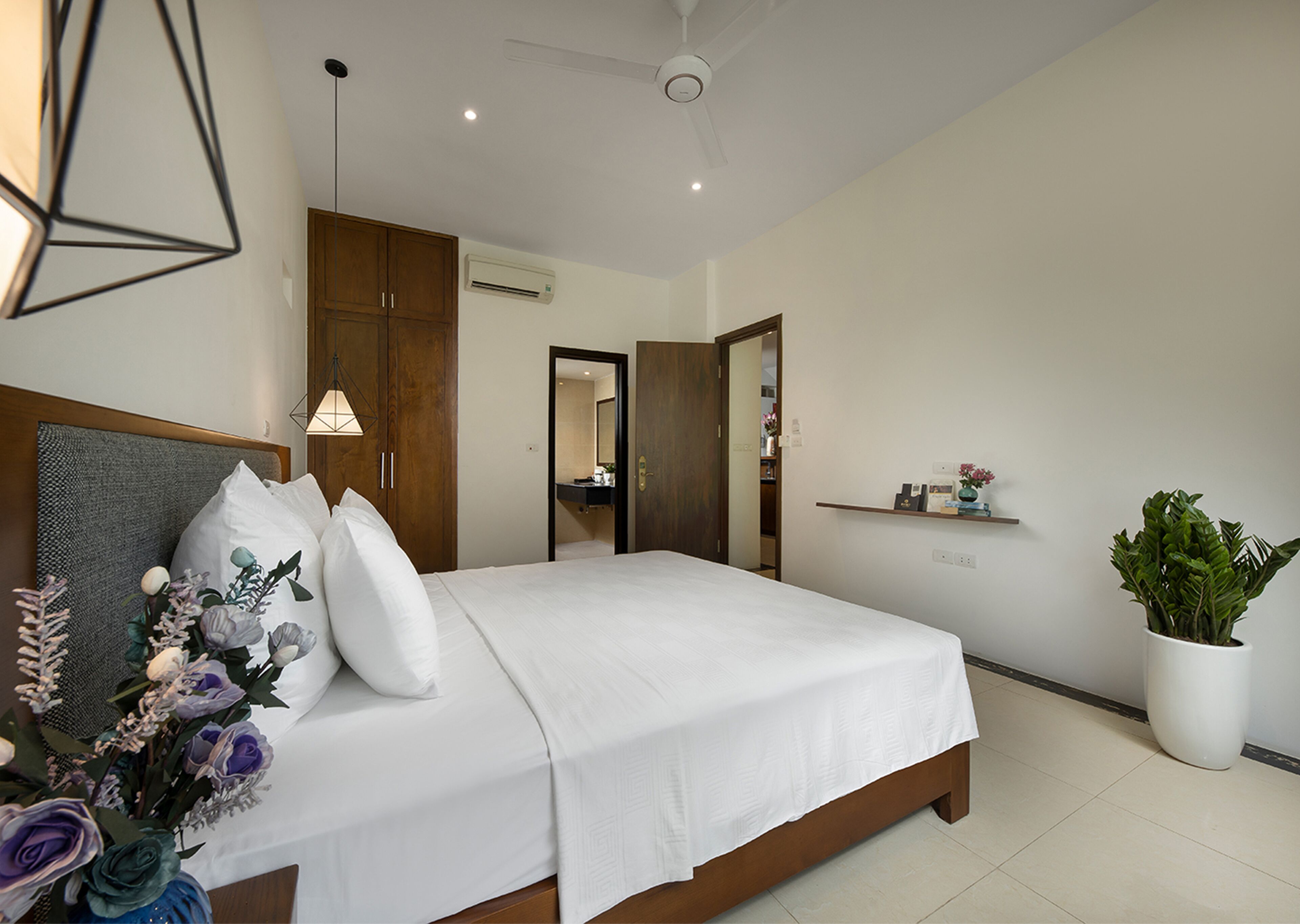 A modern bedroom with a large bed, wooden wardrobe, and a ceiling fan.