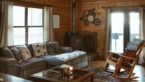 A cozy cabin interior with a wooden ceiling, a sofa, a rocking chair, a coffee table, and a fireplace. - Mt. Sherman Cabin - Ozark Mountains (Jasper)