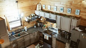 A wooden-paneled kitchen with a central island, built-in appliances, and a dining area with chairs. - Mt. Sherman Cabin - Ozark Mountains (Jasper)