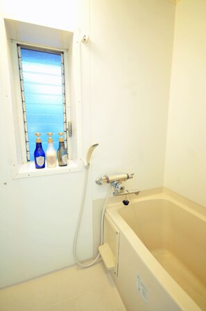 A bathroom with a bathtub, a window with bottles, and a shower hose. - Condominium House Ten-roku (Osaka)