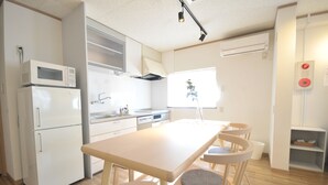 A compact kitchen with white appliances, a wooden dining table, and chairs. - Condominium House Ten-roku (Osaka)