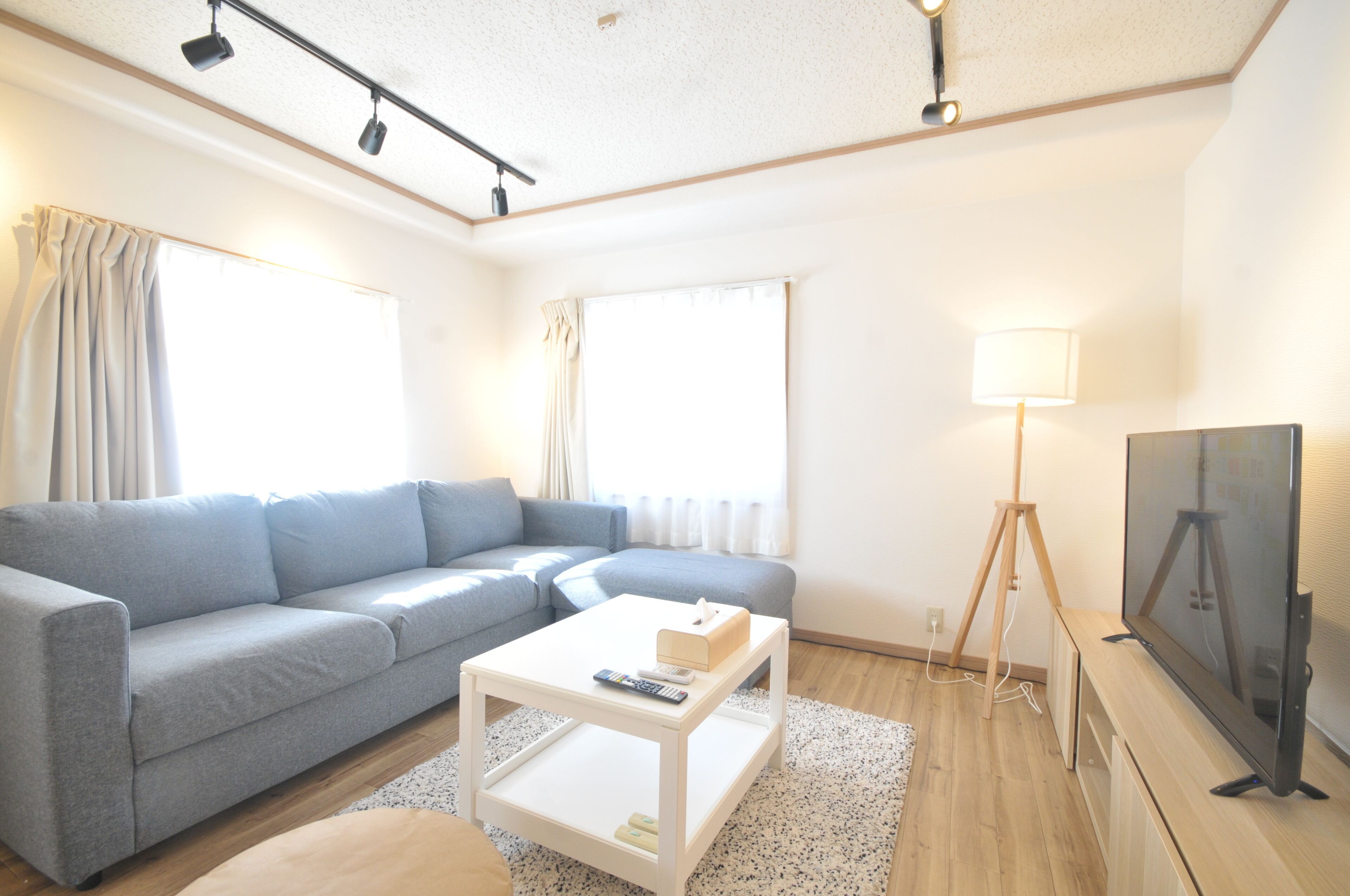 A modern living room with a grey sofa, a white coffee table, a television, and a lamp.