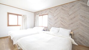 A room with two beds, wooden flooring, and a herringbone-patterned wall. - Condominium House Ten-roku (Osaka)