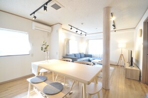 A modern living room with a dining area, a sofa set, and a television. - Condominium House Ten-roku (Osaka)