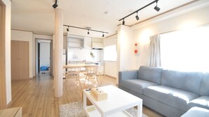A modern living room with a grey sofa, a white coffee table, and a kitchen in the background. - Condominium House Ten-roku (Osaka)