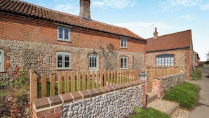 Une maison en briques avec un mur de pierres, une clôture en bois et un ciel dégagé.