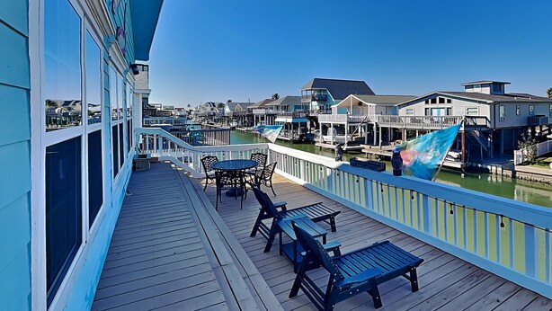 A wooden deck with outdoor furniture, a view of a marina, and buildings in the background. - Canal-Front Home, 2-Min Drive to Beach, Fishing Pier. (Galveston)