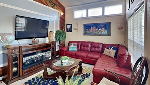 A living room with a red leather sofa, a wooden coffee table, a television, and a globe on a wooden cabinet. - Canal-Front Home, 2-Min Drive to Beach, Fishing Pier. (Galveston)