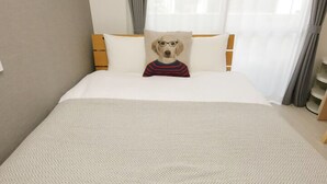 A hotel room with a bed, a pillow with a dog face, and a window with curtains.