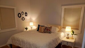 Een net opgemaakt bed met wit beddengoed, twee nachtkastjes met lampen en een kleine plant op een van de tafels.