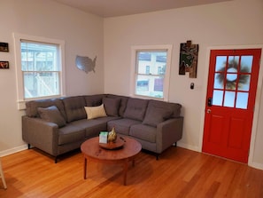 A living room with a sectional sofa, a round coffee table, and a red door.