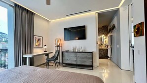 A modern hotel room with a large bed, a desk, a chair, a TV mounted on the wall, and a view of the city through the window. - Casa Frida: Luxe Pier 57 Oceanview Corner Unit (Puerto Vallarta)