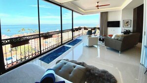A spacious living room with a balcony overlooking the ocean, a sofa, a coffee table, and a TV. - Casa Frida: Luxe Pier 57 Oceanview Corner Unit (Puerto Vallarta)