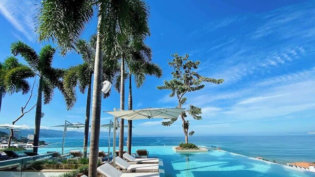A poolside area with lounge chairs and umbrellas, overlooking a clear blue ocean. - Casa Frida: Luxe Pier 57 Oceanview Corner Unit (Puerto Vallarta)