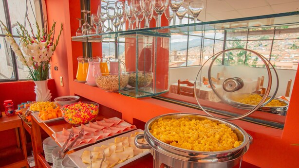 A buffet with various food items, including a large pot of yellow rice, bowls of cereal, and trays of sliced meats. -  HOTEL MOSOQ KILLA (Cusco)