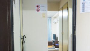 Un pasillo con un cartel de prohibido fumar, una puerta con manija, un par de pantuflas en el suelo y un televisor al fondo.