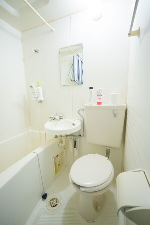 A small, white bathroom with a bathtub, sink, toilet, and a mirror above the sink. - Uzumasa 102 (Kyoto)