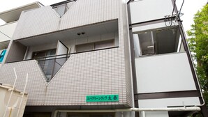 Un edificio moderno con fachada de baldosas, un balcón visible y un letrero verde con texto japonés.