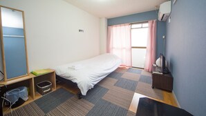 A small, neatly arranged bedroom with a single bed, a desk with a computer, a chair, and a window with curtains. - Uzumasa 201 (Kyoto)