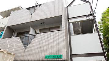A modern building with a tiled facade, a visible balcony, and a green sign with Japanese text.