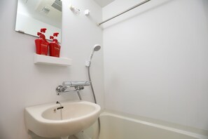 A bathroom with a white sink, a mirror, and a shower. There are two red bottles on a shelf above the sink.