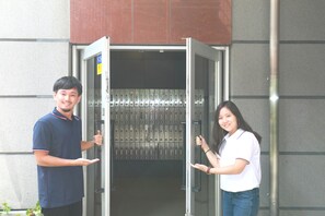 A man and a woman standing in front of a metal door with a glass panel, possibly a hotel entrance or office.