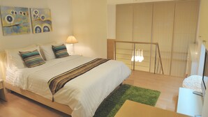 Un dormitorio moderno con una cama grande, una alfombra verde y un televisor, además de una obra de arte en la pared.
