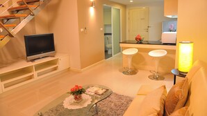 Una sala de estar moderna con televisor, una mesa de centro de vidrio con un jarrón, sofá y una escalera.