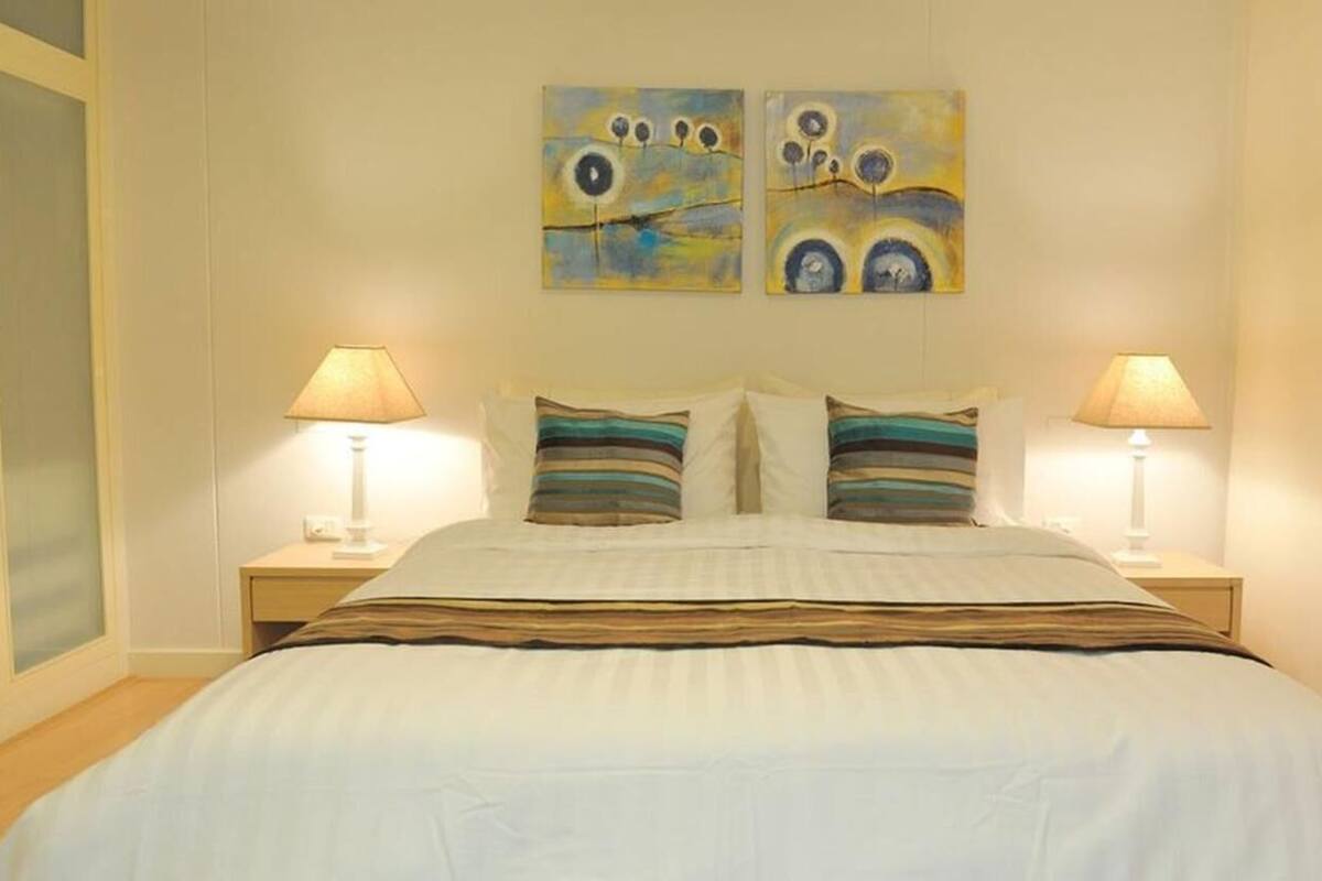A neatly made bed with striped bedding, two bedside lamps, and two abstract paintings on the wall.