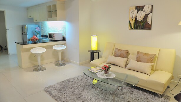 Una sala de estar moderna con una mesa de centro de vidrio, un sofá y dos taburetes blancos.