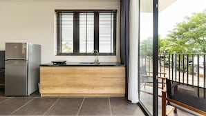 Une cuisine moderne dotée d’un réfrigérateur encastré, de meubles en bois, d’un plan de travail noir et d’une fenêtre avec des stores.
