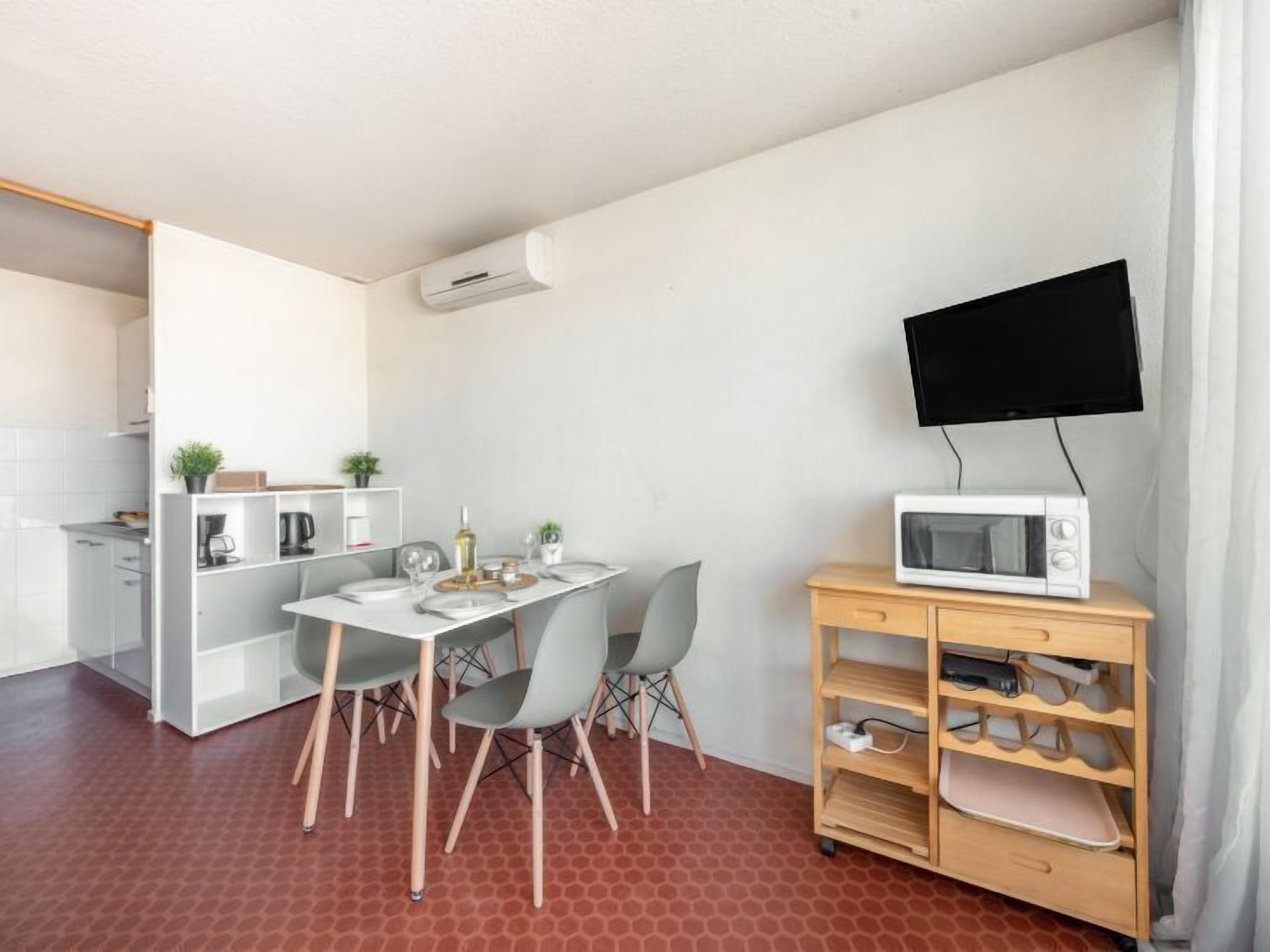 A compact living space with a kitchenette, a dining area, and a TV mounted on a wooden cabinet.