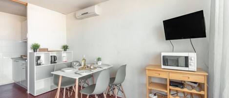 A compact living space with a kitchenette, a dining area, and a TV mounted on a wooden cabinet.