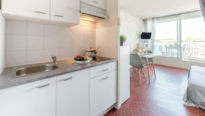 Cucina compatta con mobili bianchi, lavello in acciaio inossidabile e zona pranzo con tavolo e sedie.