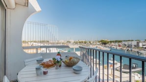 Un balcone con un tavolo bianco apparecchiato per mangiare, con vista su una marina piena di barche e un cielo azzurro terso.