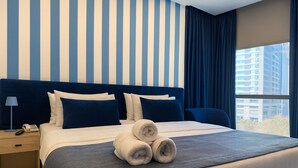 A hotel room with a large bed, striped walls, and a view of buildings through the window. - Shade Hotel Beirut (Beirut)