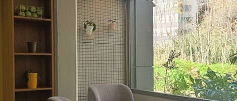 Une pièce moderne avec un canapé gris, une petite table ronde, une bibliothèque en bois et une vue sur la verdure.