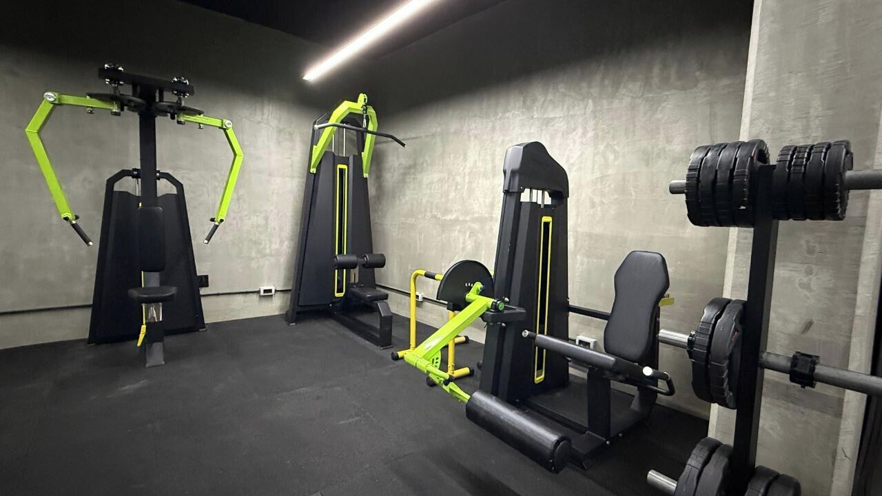 A gym with various exercise machines, including a squat rack, a bench press, and a cable machine.