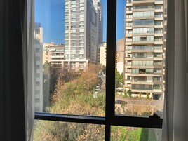 Blick durch ein Fenster mit Vorhängen, zeigt hohe Wohnhäuser und eine Straße mit geparkten Autos.