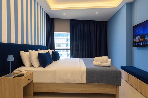 Un dormitorio de hotel moderno con una cama grande, un escritorio, un televisor de pantalla plana y vistas a la ciudad.