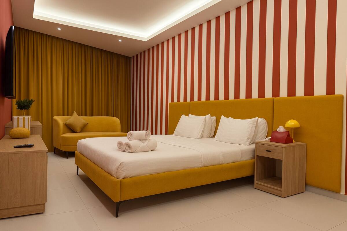 A modern hotel room with a large bed, a sofa, a bedside table, and a TV.