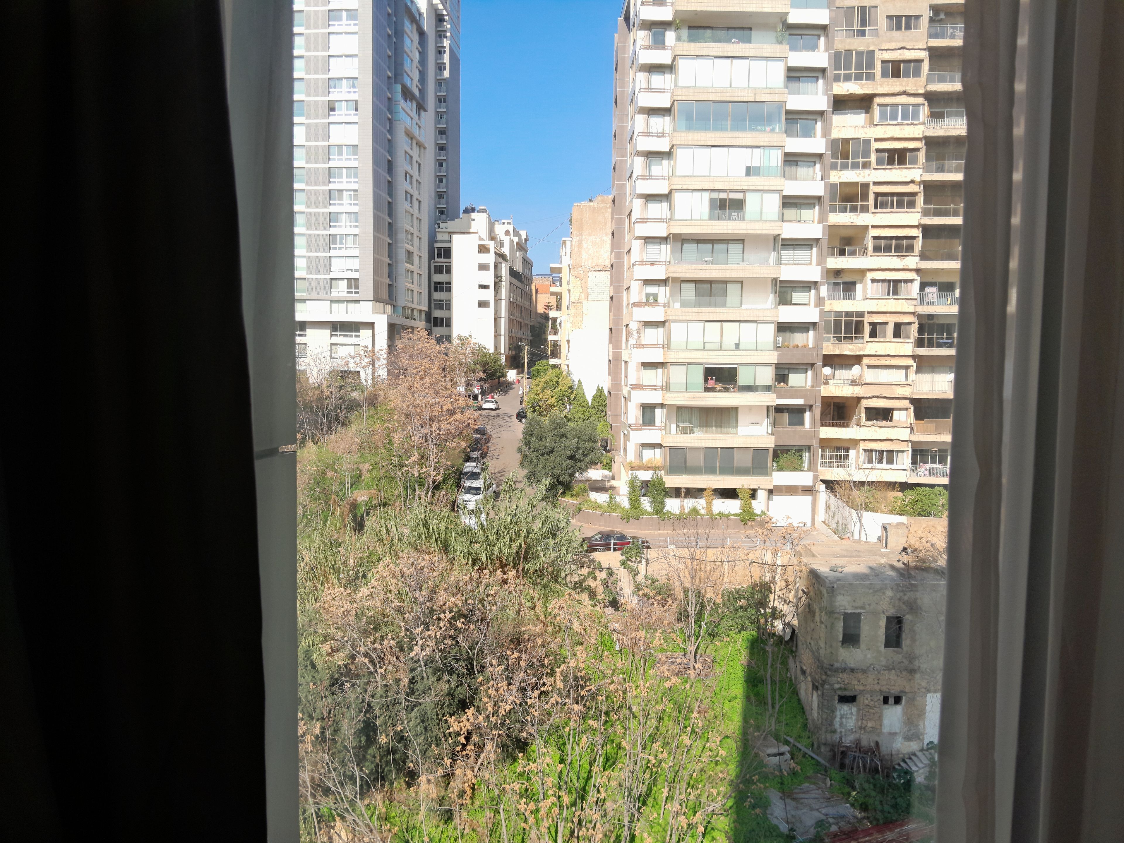 A view of a residential area with tall apartment buildings, a narrow street, and some greenery.