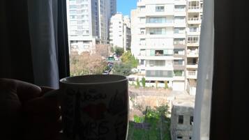 A hand holding a mug with writing and a heart, through a window overlooking high-rise buildings.