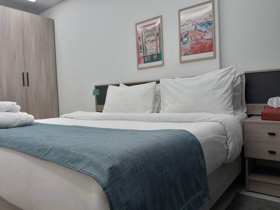 Un letto rifatto con lenzuola bianche e una coperta turchese, un armadio in legno e due opere d'arte incorniciate appese al muro.