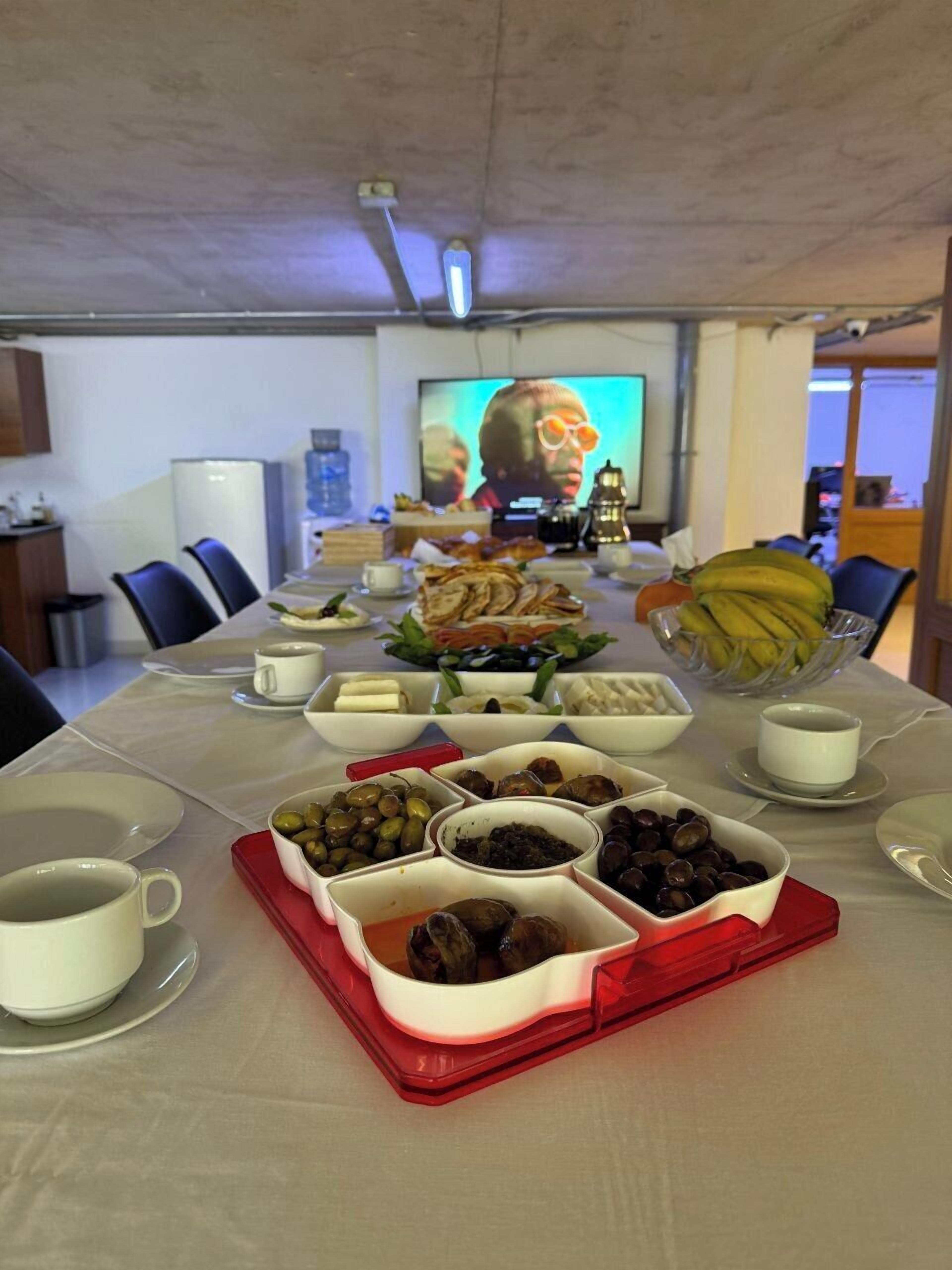 Un salón de conferencias con una larga mesa dispuesta para una reunión, equipado con un proyector y una pantalla grande.